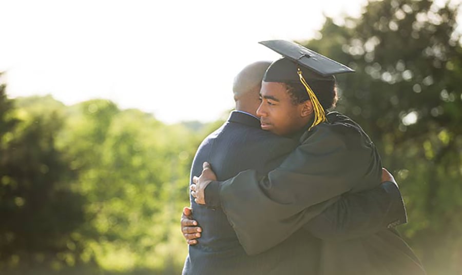 Student in graduation robe hugging family